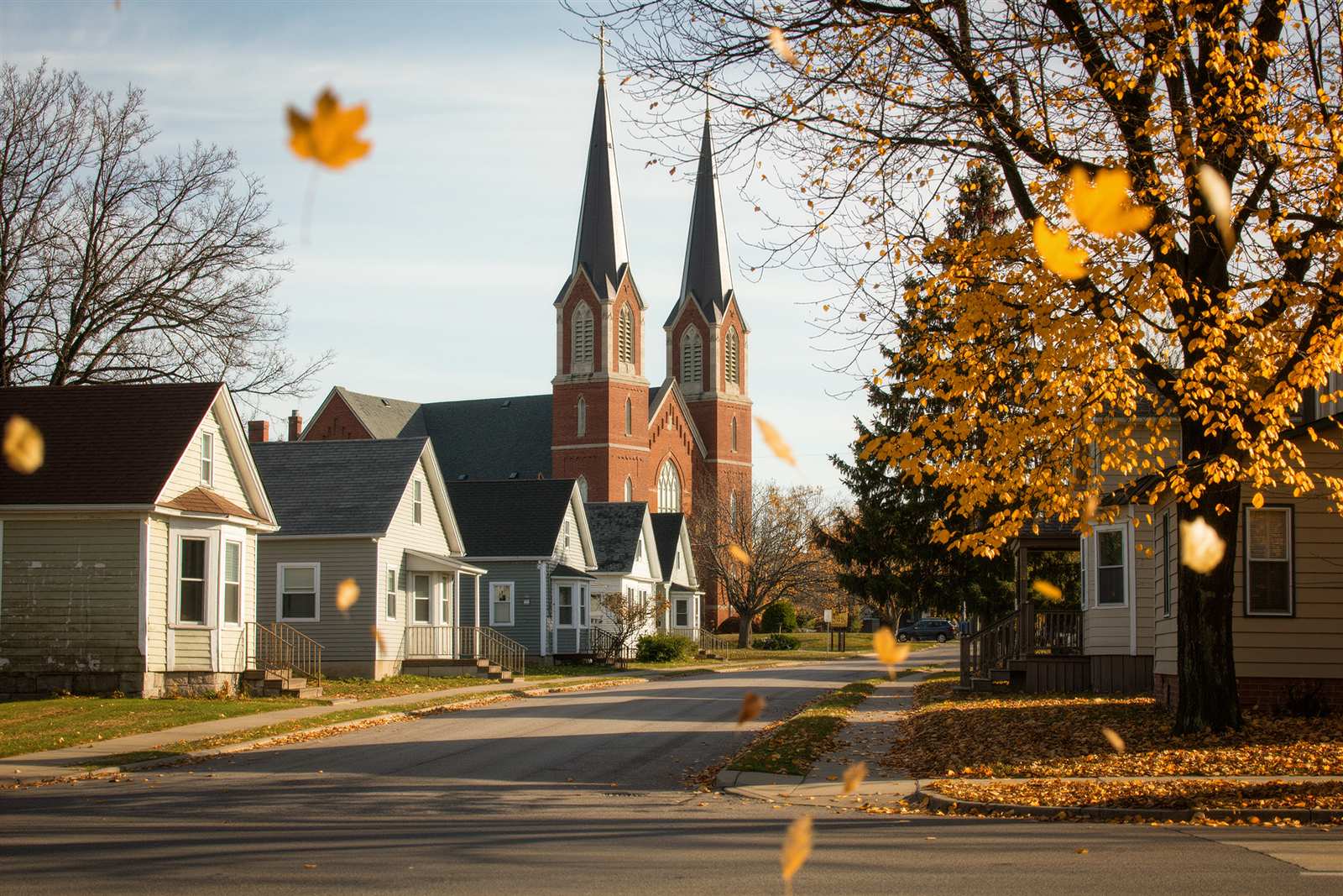 A street of small wood-frame houses with a twin-spire brick church in the background